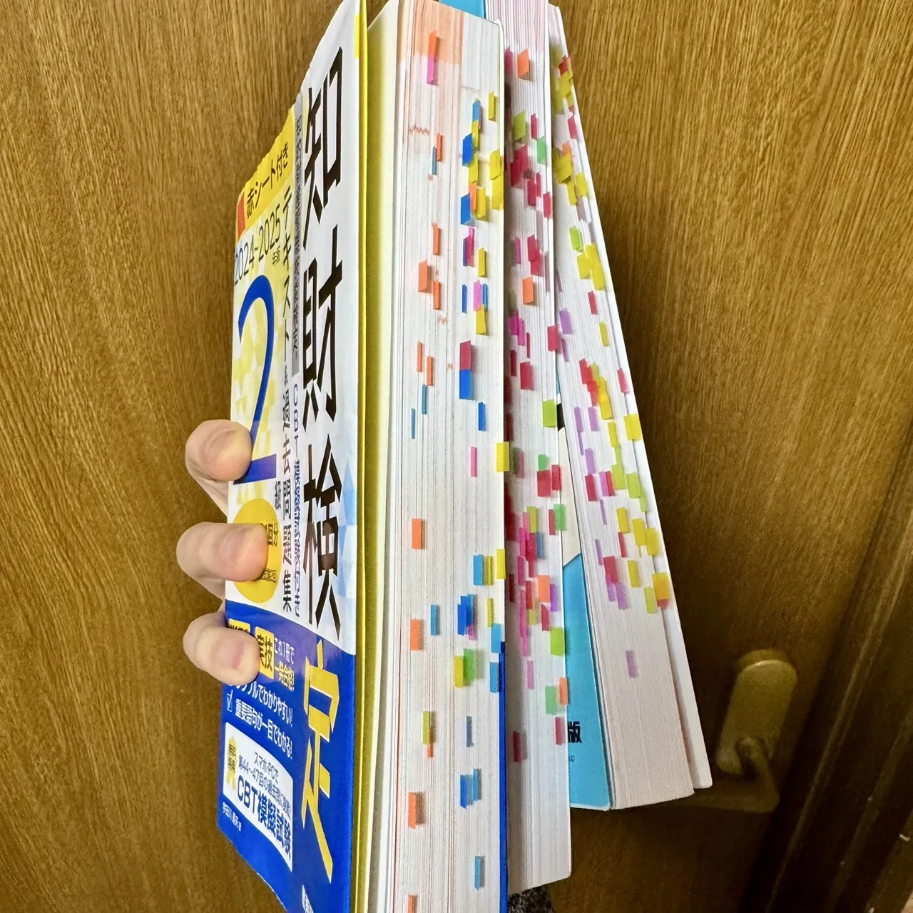 付箋をたくさん貼った知的財産管理技能検定2級のテキストと問題集を手に持っているところ。